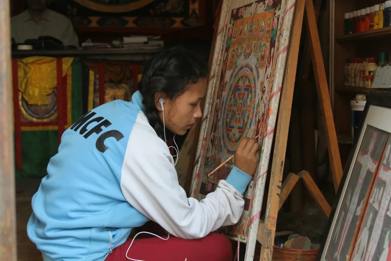 Painting an intricate traditional Thangka mandala artwork on a canvas mounted on a wooden easel.