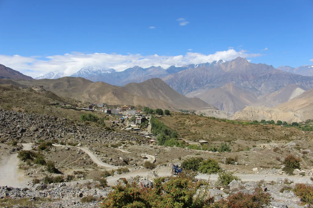 Scenic view of Ranipauwa village in the arid Muktinath Valley of Mustang, Nepal, with the snow-capped Himalayan mountain range under a blue sky.