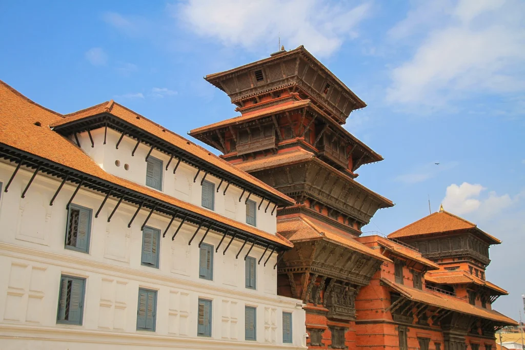 A side-angle view of the historic Hanuman Dhoka royal palace complex in Kathmandu Durbar Square under a blue sky with light clouds.